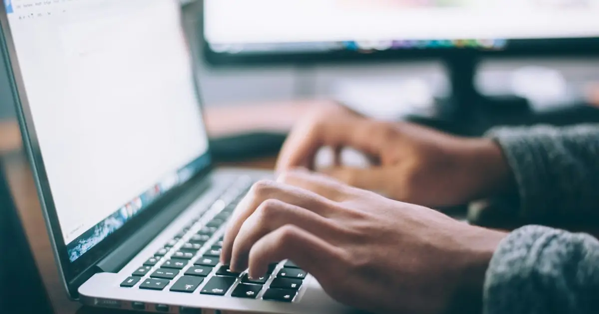 Osoba pisząca na laptopie przy oknie